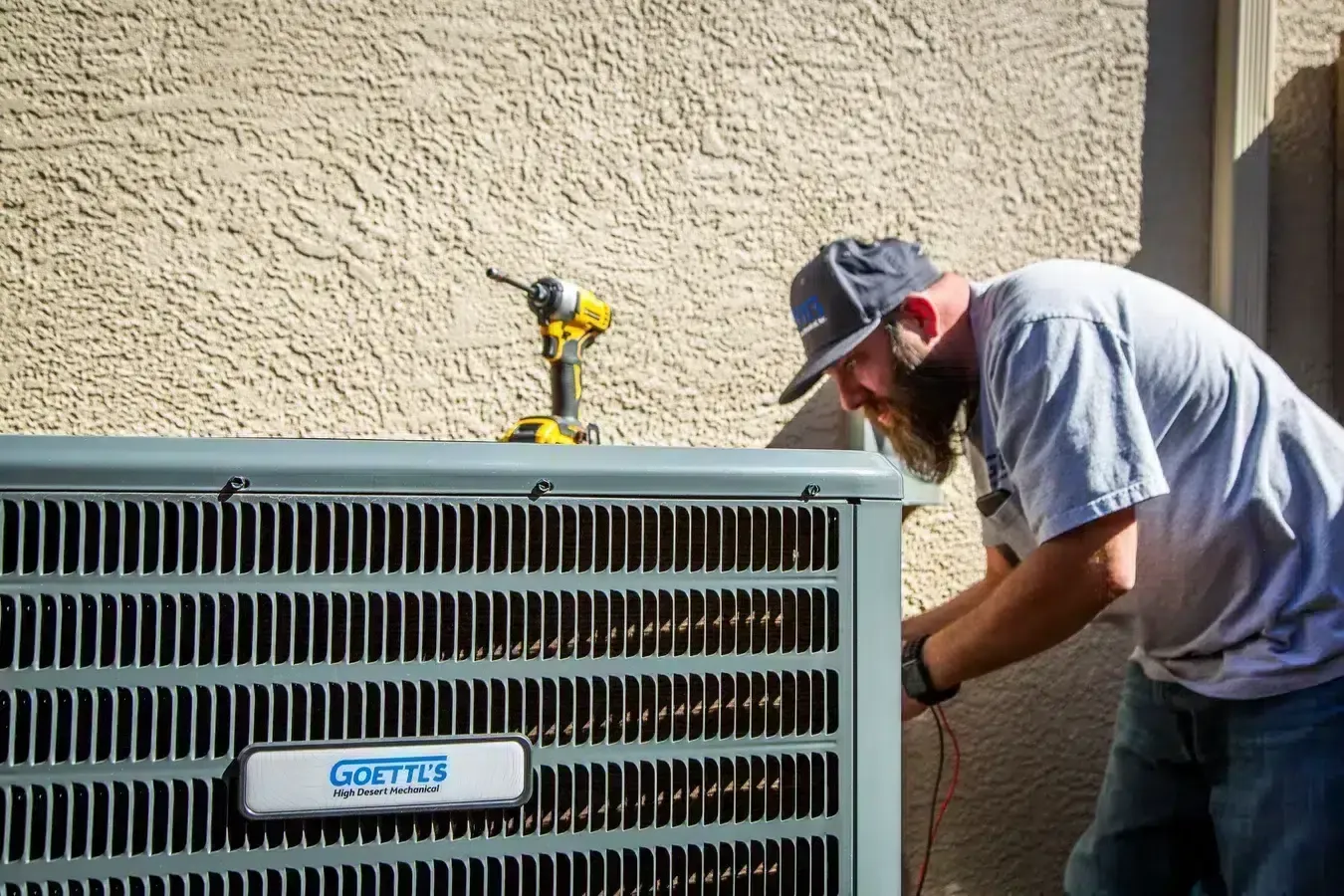 Goettl’s High Desert Mechanical technician servicing outdoor condenser unit beside home – Prescott Valley AZ