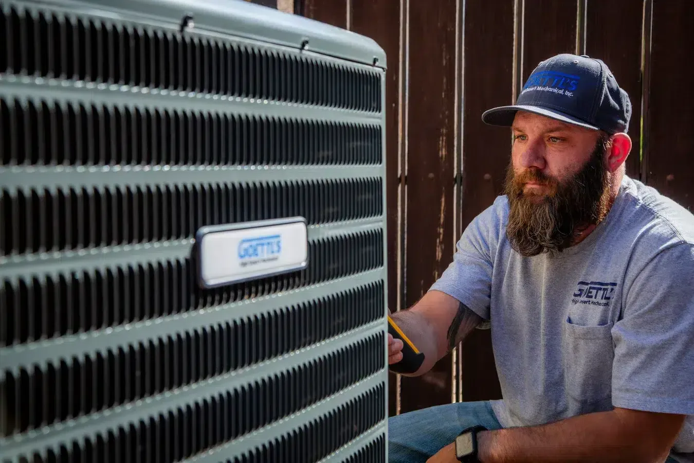 Goettl’s High Desert Mechanical technician kneeling beside condenser performing system check – Prescott Valley AZ