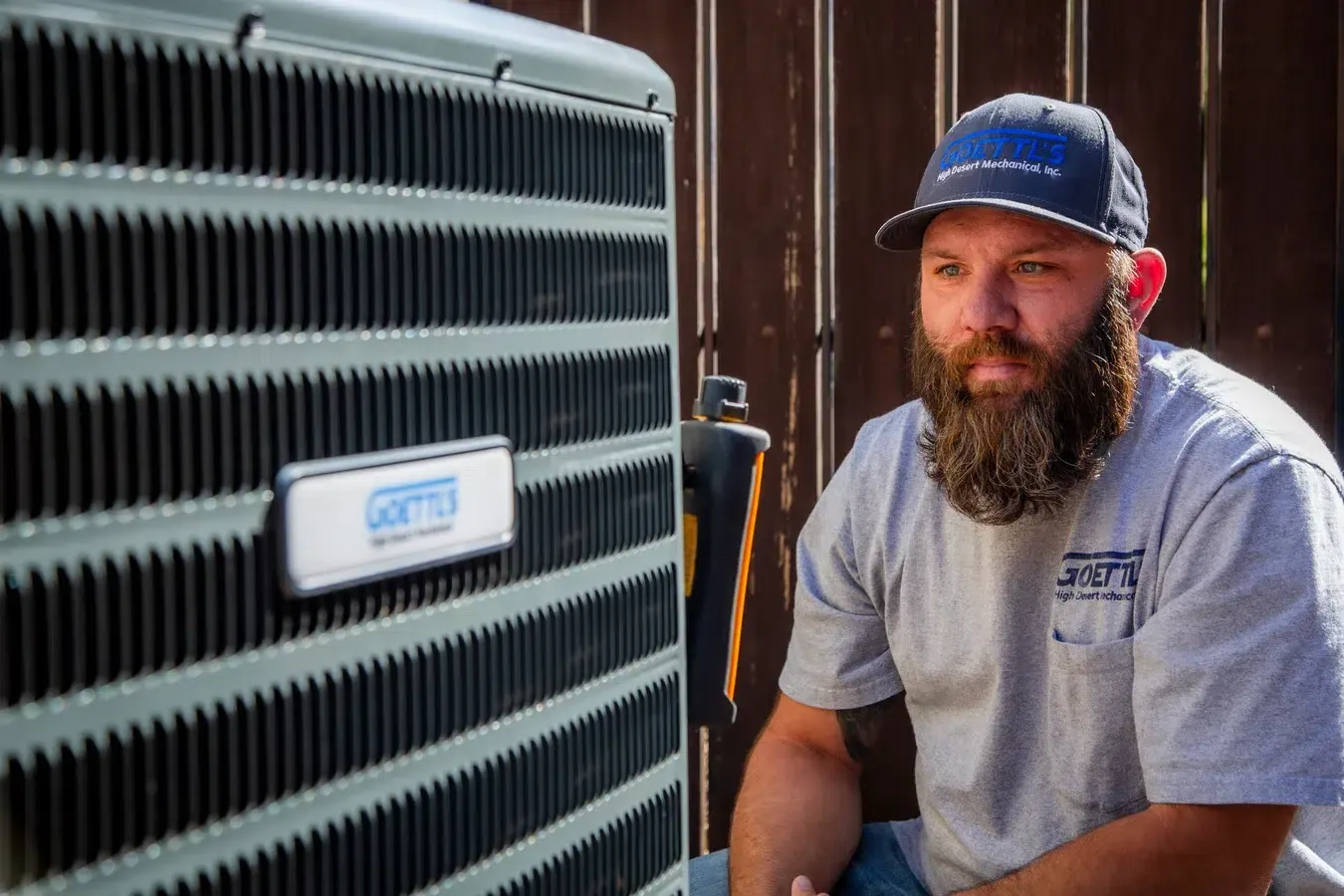 Goettl’s High Desert Mechanical technician kneeling beside condenser unit during system inspection – Prescott Valley AZ