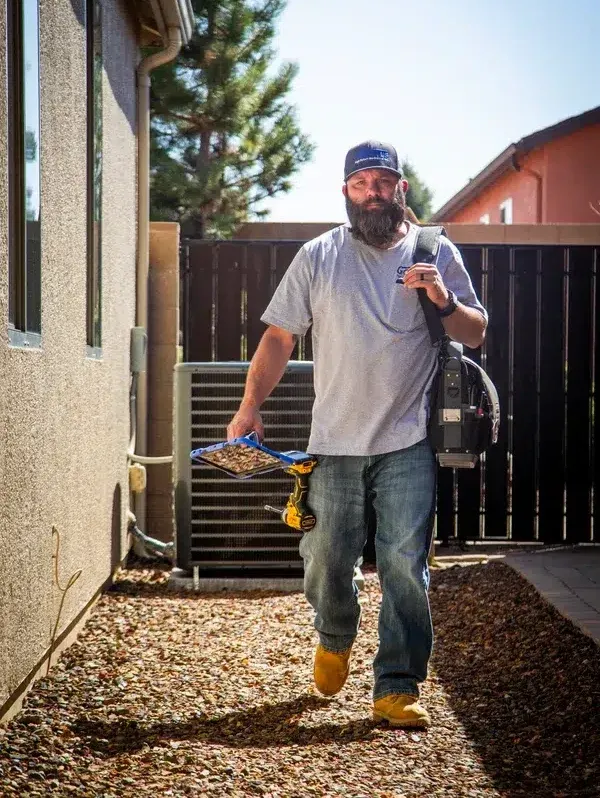 Goettl’s High Desert Mechanical technician walking toward side-yard condenser unit with tools – Prescott Valley AZ