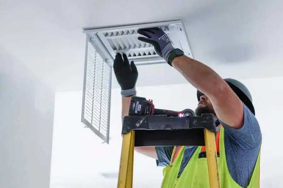 Technician installing or adjusting ceiling supply vent grille from ladder – Goettl’s High Desert Mechanical Prescott Valley AZ