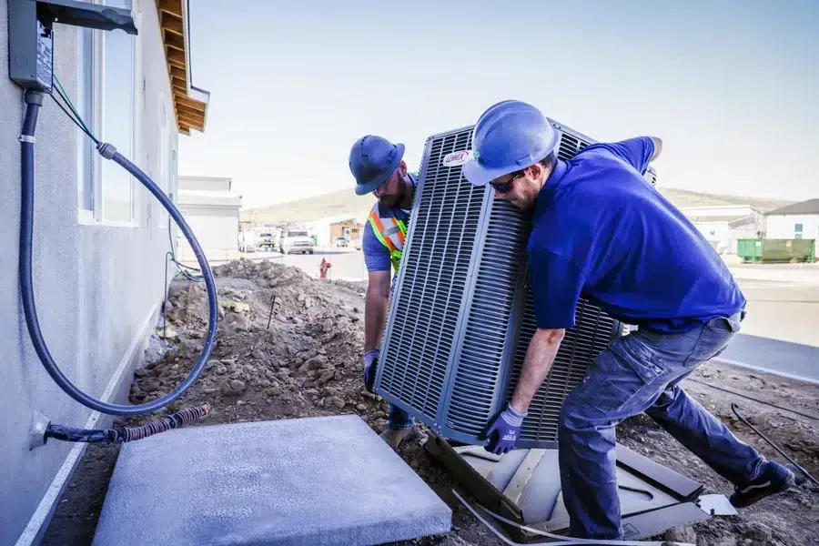 Technicians lifting and positioning outdoor HVAC condenser on jobsite – Goettl’s High Desert Mechanical Prescott Valley AZ
