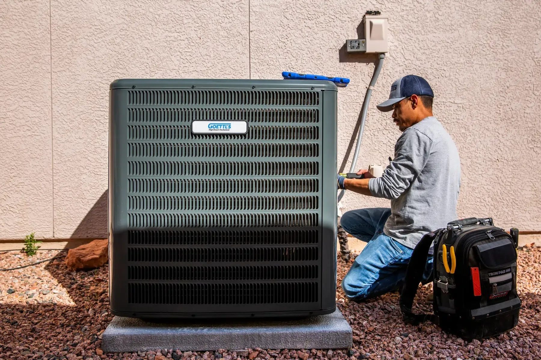 Goettl’s High Desert Mechanical technician servicing outdoor HVAC unit beside home – Prescott Valley AZ