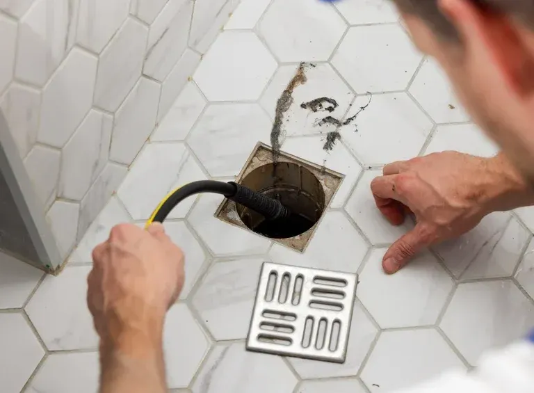 Plumber unclogging blocked shower drain with hydro jetting