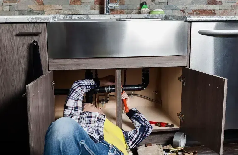 Plumber repairing pipe under kitchen sink in Prescott Valley, AZ.