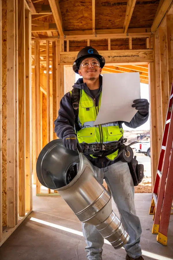 Goettl’s High Desert Mechanical technician carrying metal duct pipe through new construction framing – Prescott Valley AZ