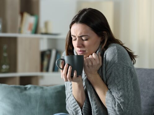 Woman shivering on a couch while holding a coffee cup